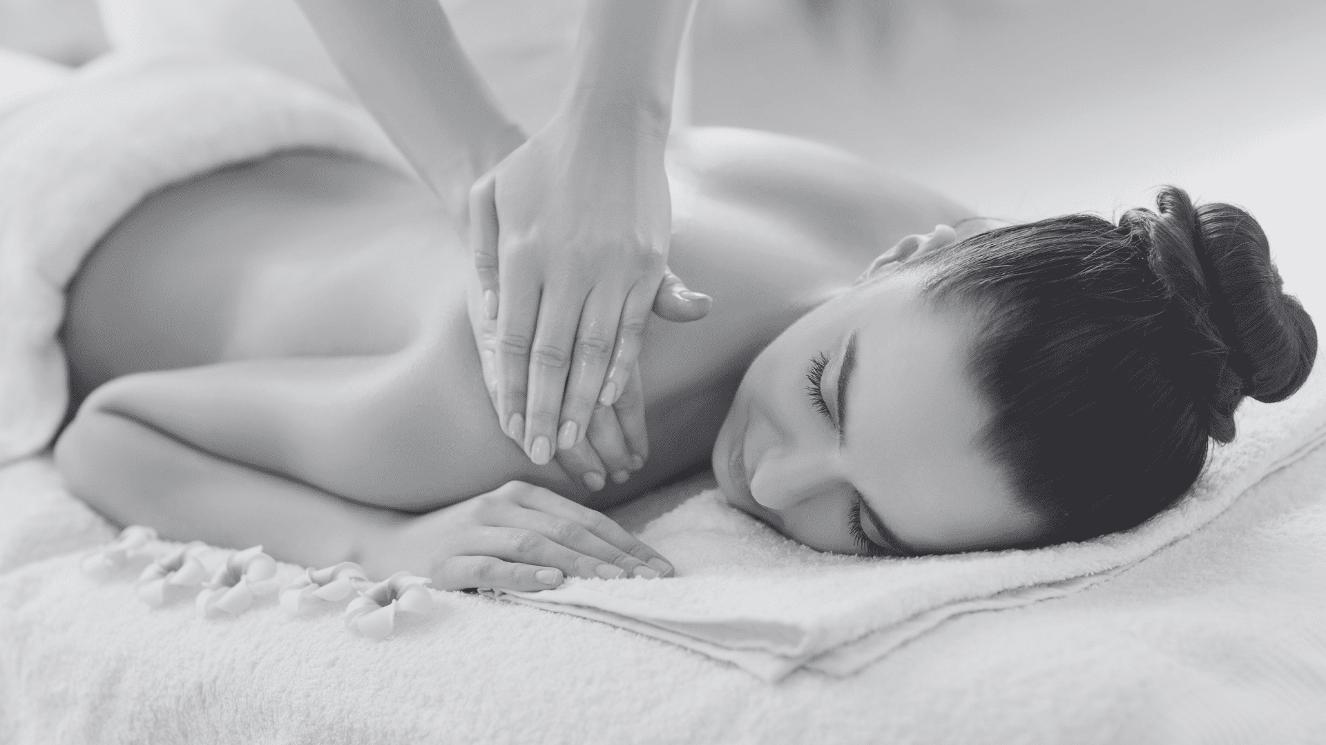 Woman receiving a back massage at a spa, surrounded by folded towels and flower petals.