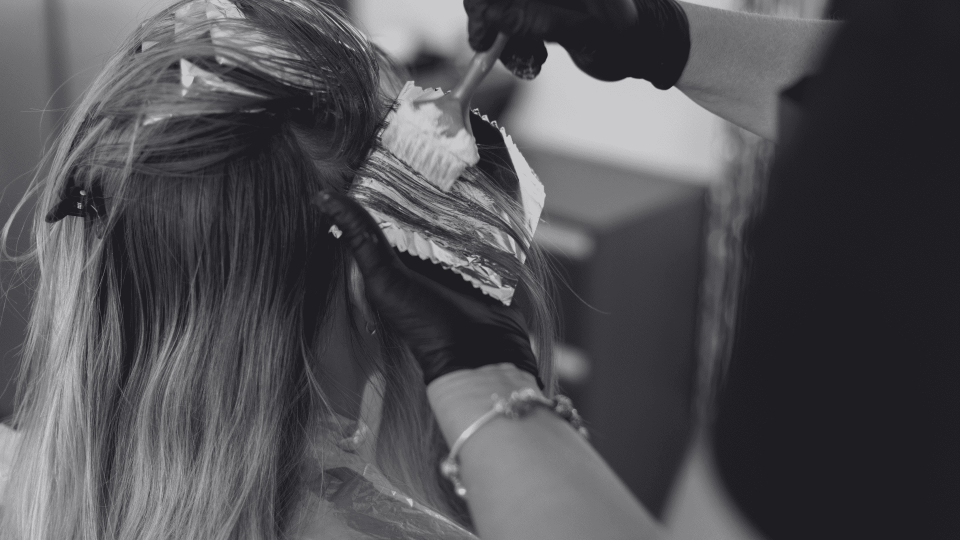 Hairdresser applying color to woman's hair with brush and foil.