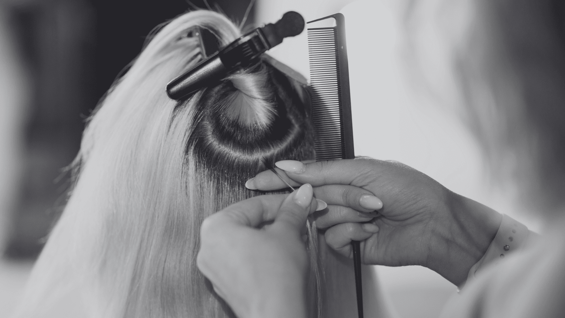 Hair stylist parts blonde hair and uses a straightener and comb. Close-up of hands and tools.