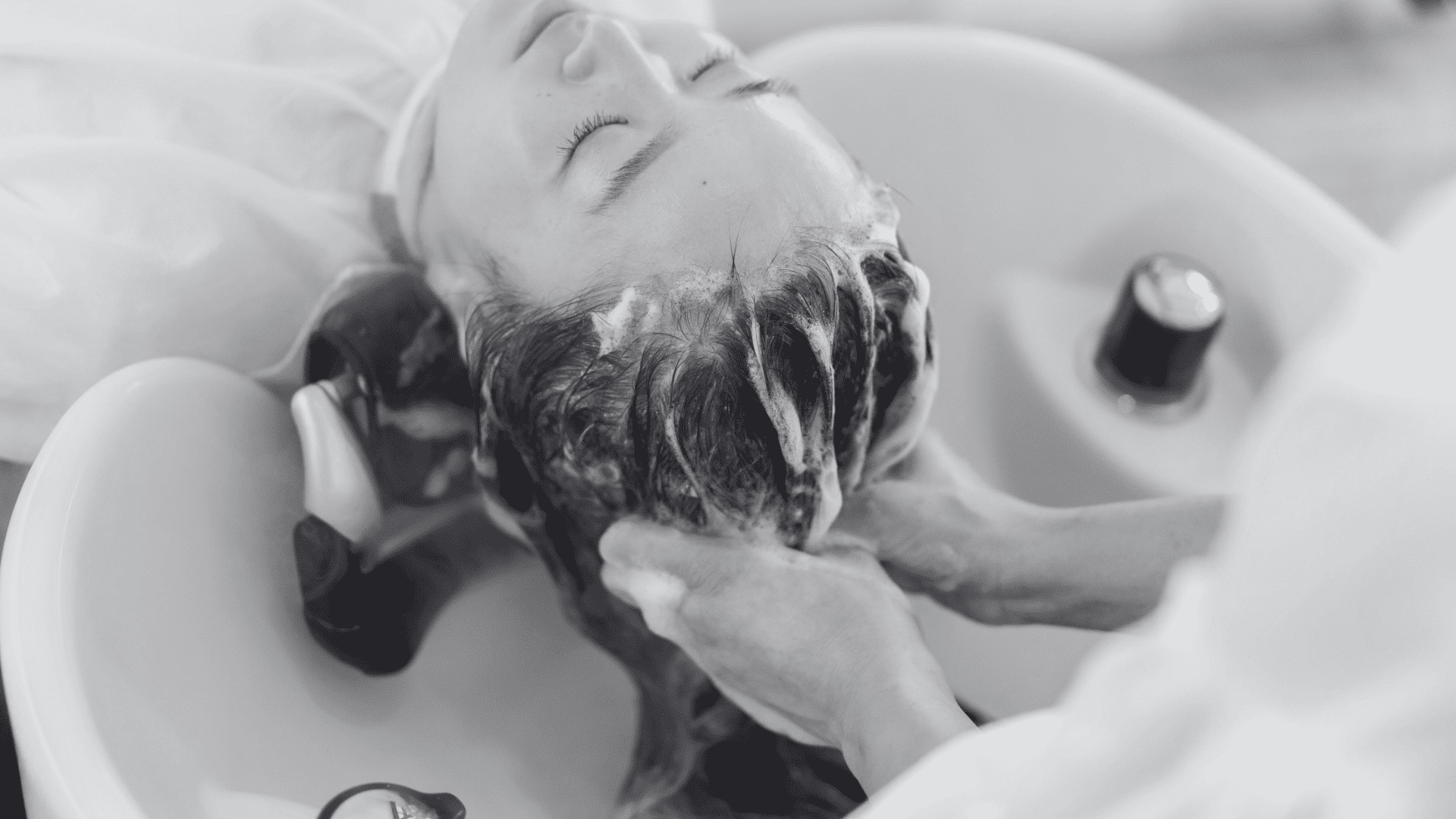 Person getting their hair washed in a salon sink, eyes closed, enjoying the relaxing experience.