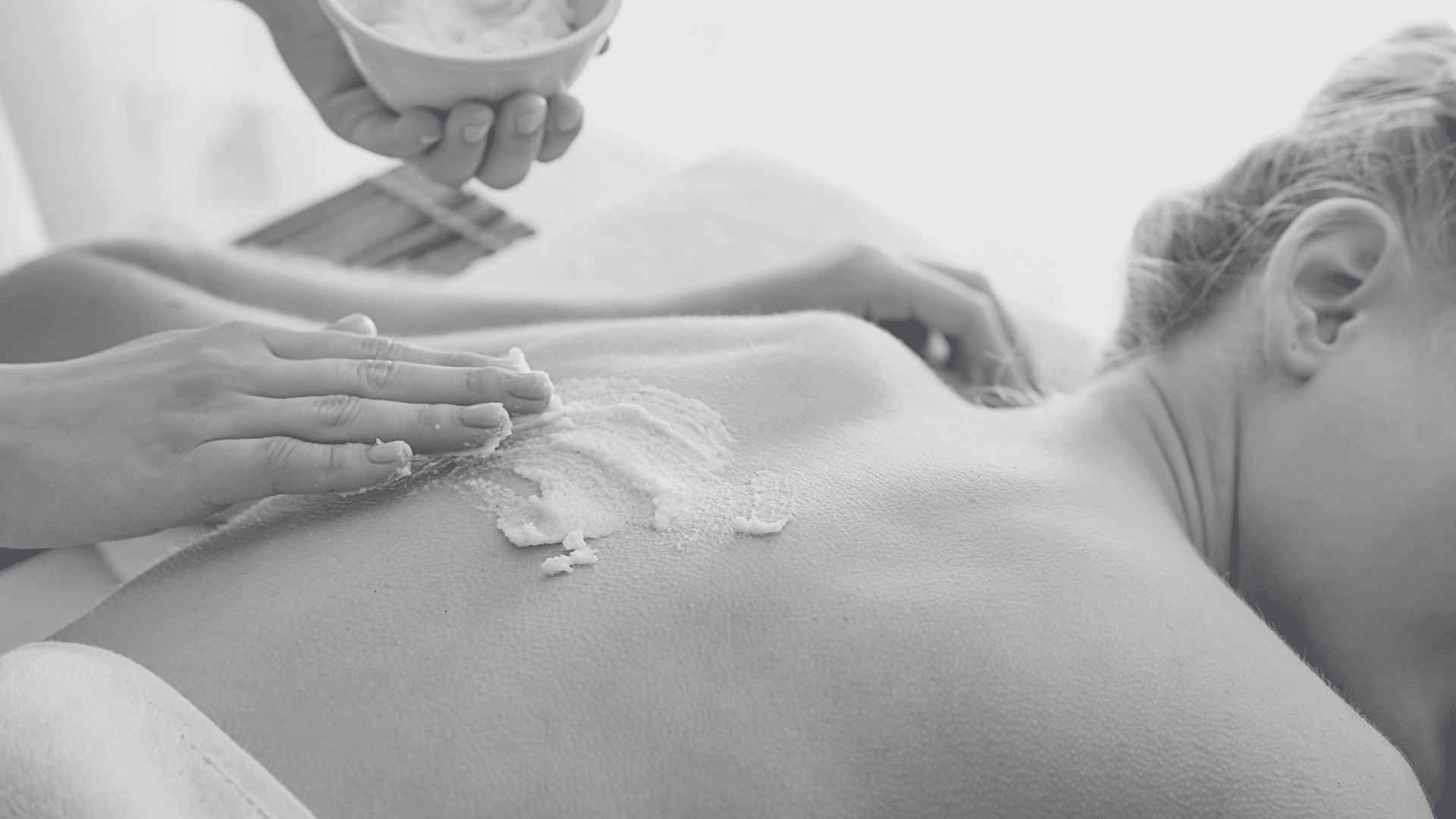 Person receiving a spa treatment with cream applied on their back. Relaxing atmosphere.