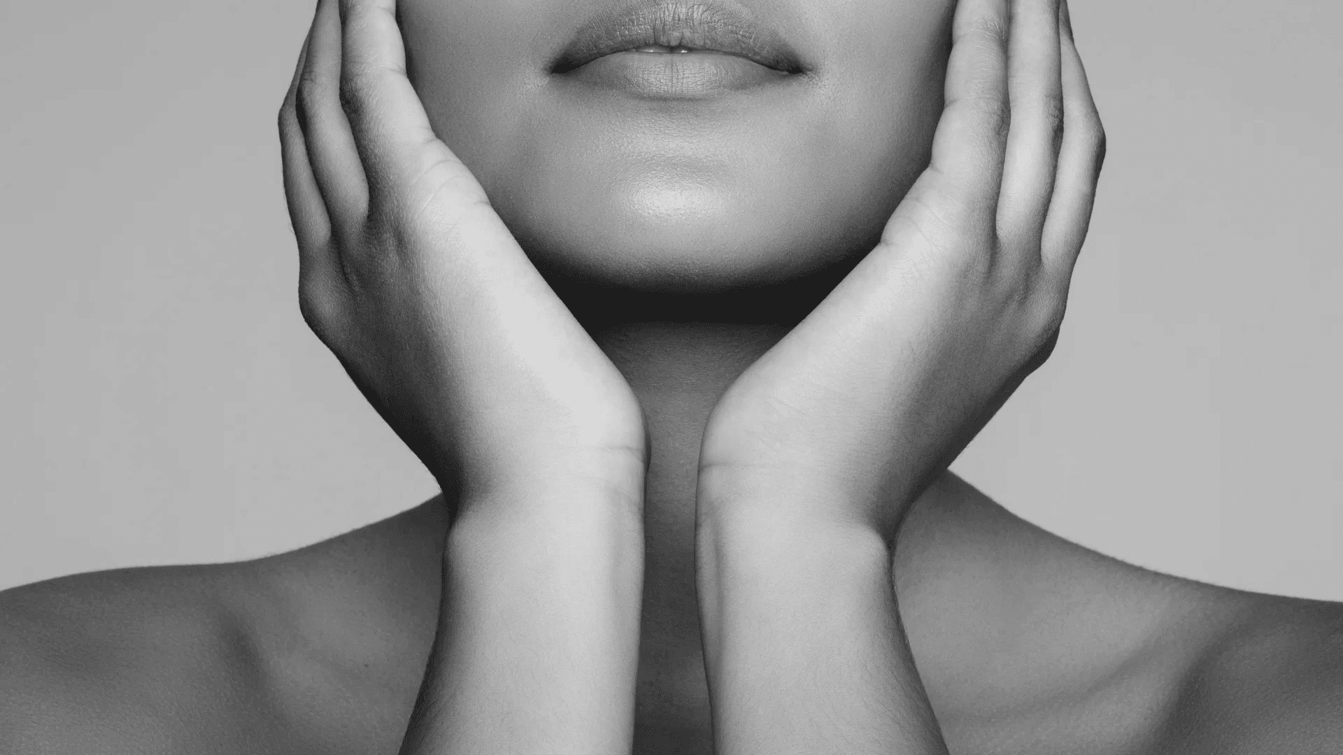 Woman touching her face with both hands, showing smooth skin and subtle makeup.