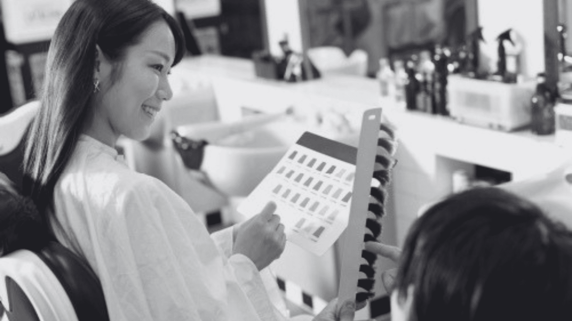 Woman in salon choosing nail polish color from a selection card, smiling at technician.