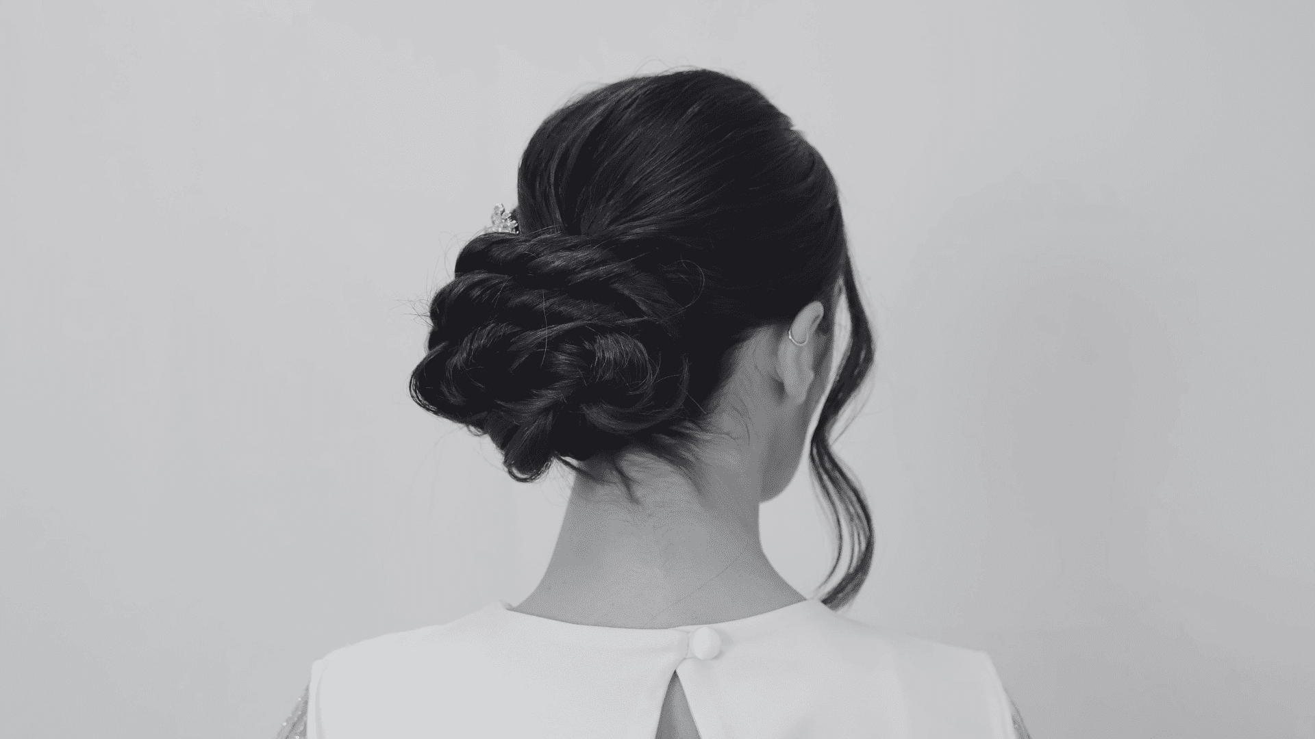 Back view of a woman with an elegant braided updo hairstyle, wearing a white top.
