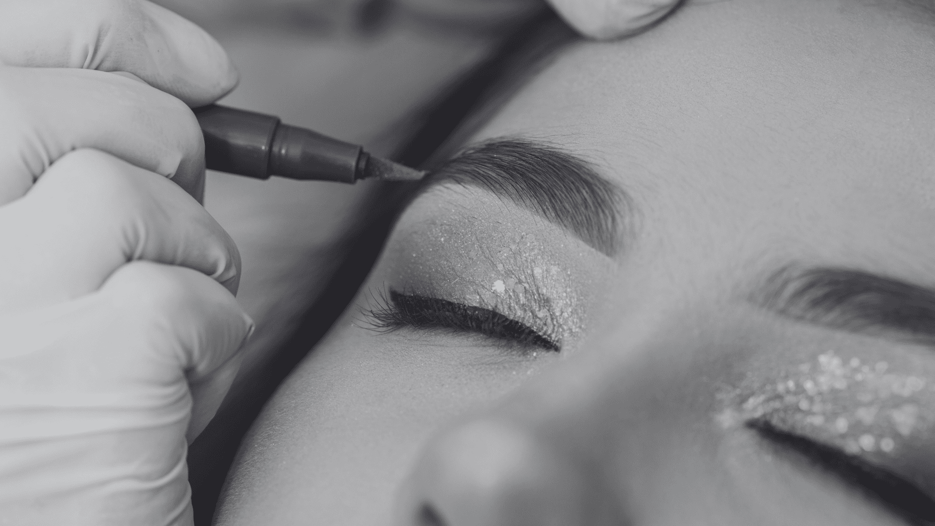 Close-up of a person receiving a cosmetic eyebrow enhancement with a pen, eyes closed.