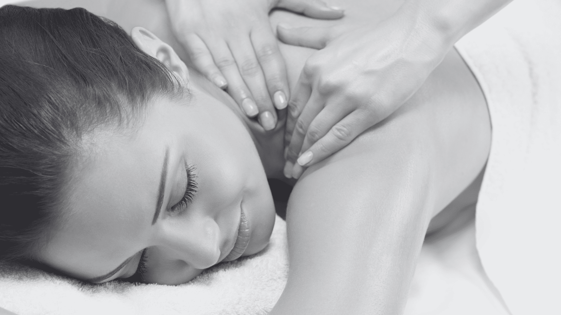 Person receiving a relaxing back massage, lying face down with eyes closed on a white towel.
