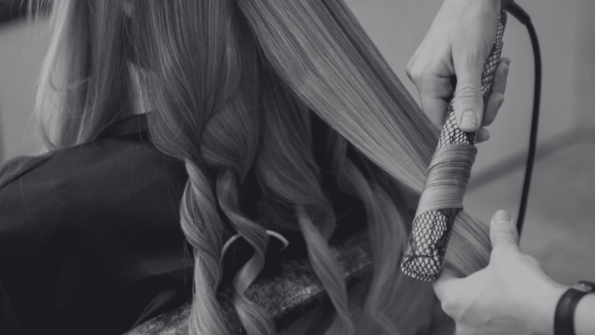 Hair being styled with a curling iron by a hairdresser, creating waves in long, straight hair.