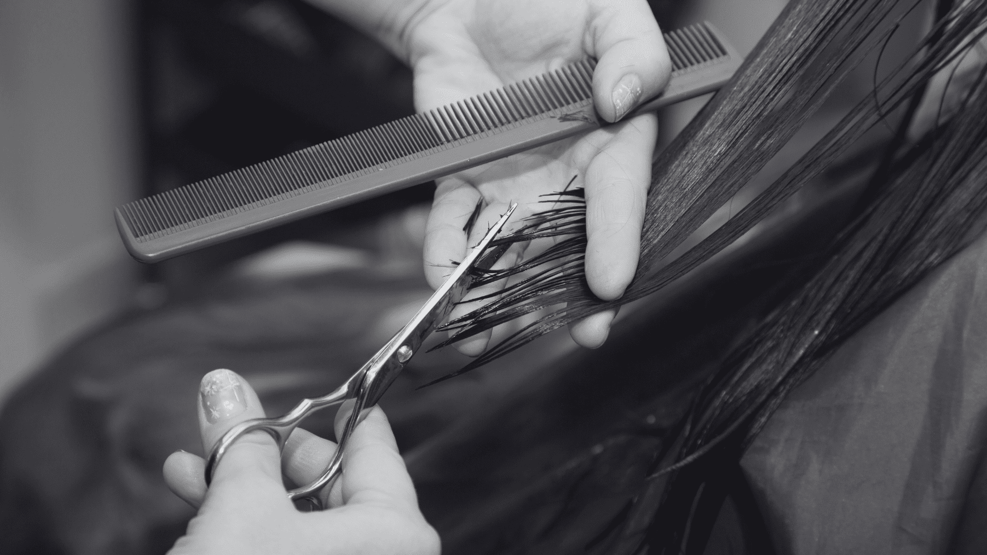 Scissors trim long hair guided by a comb, held by a person in a hair salon setting.